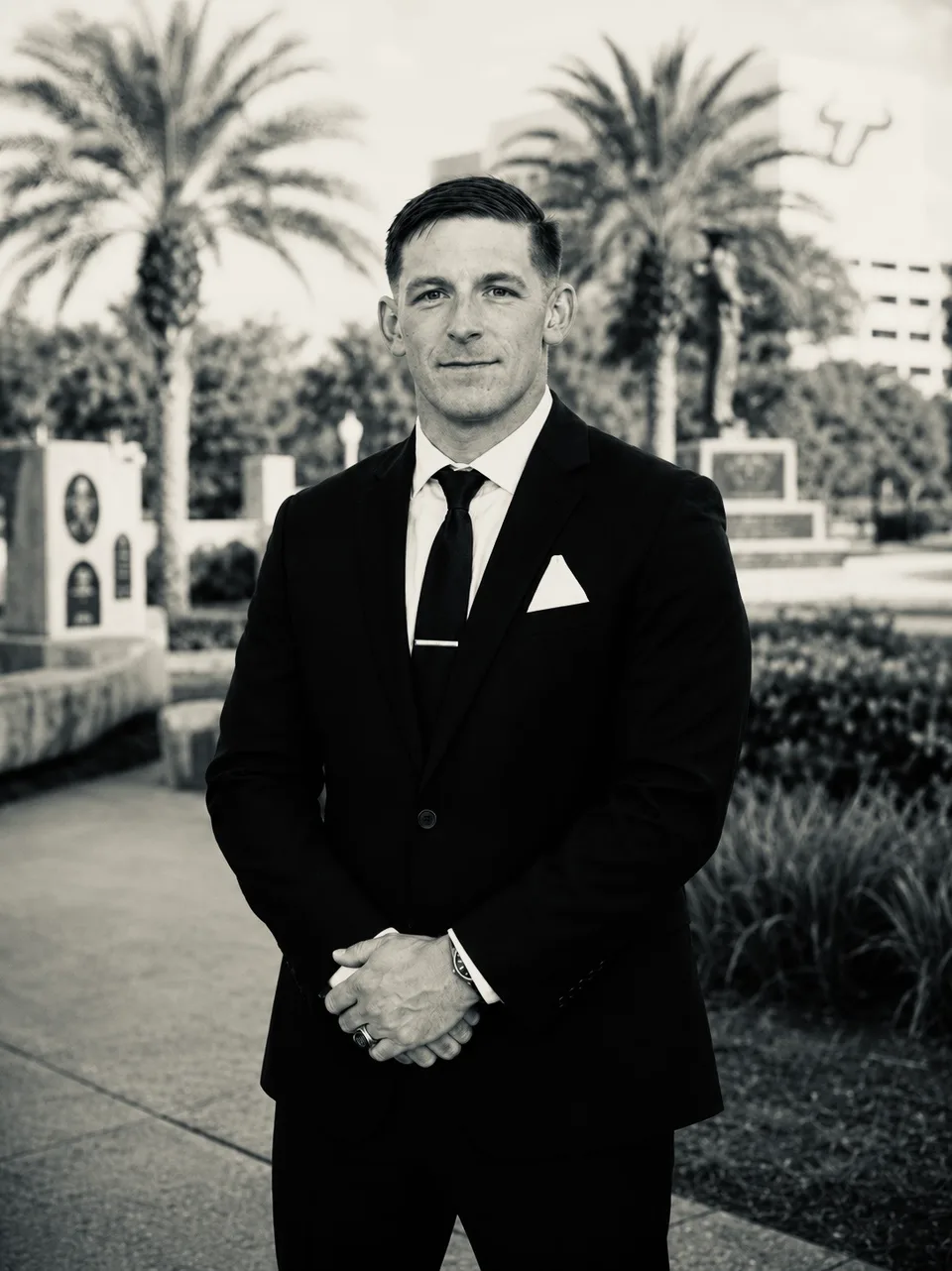 Ryan Powers in a dark suit, standing outdoors among palm trees